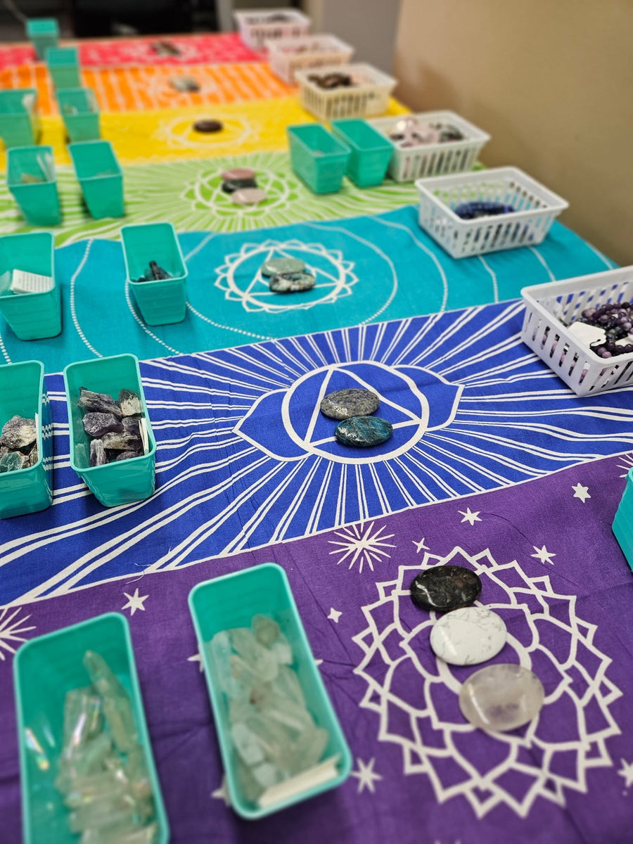 Crystals arranged by chakra on a rainbow tapestry at a necklace workshop
